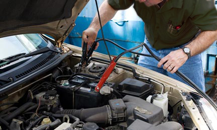 Mechanic is applying jumper cables to the battery of a car